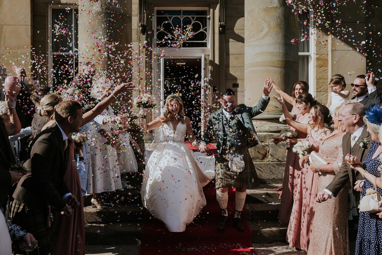 bride and groom have lots of colourful confetti thrown over them by guests